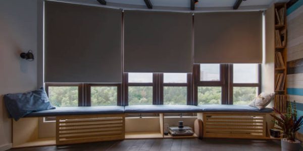 elektrische gordijnen Motorized roller shades in the interior. Automatic roller blinds blackout fabric on large windows. Remote Control Shades are above the windosill with pillows. Summer. Green trees outside.
