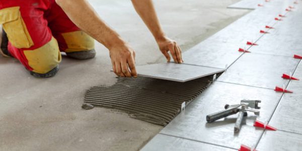 nivellering Ceramic Tiles. Tiler placing ceramic wall tile in position over adhesive with lash tile leveling system - Image